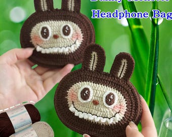 Könnte beinhalten: Zwei braune Häkeltaschen für Kopfhörer mit einem Bunny-Monster-Design werden hochgehalten. Die Taschen haben ein weißes Gesicht, rosa Wangen und einen lächelnden Mund. Der Text "Bunny Monster Headphone Bag" befindet sich im Hintergrund. Garn befindet sich in der unteren linken Ecke.