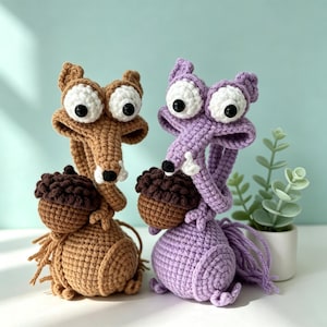 May include: Two crochet squirrel figures, one brown and one purple, each clutching a brown acorn. The squirrels have large, expressive eyes and long, curved snouts. The figures are handmade and sit on a white surface against a light teal background.