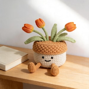May include: A handmade crochet flower pot with orange tulips. The pot is beige with a brown top and has a smiling face. The pot has two small brown legs. The tulips have green stems and leaves.