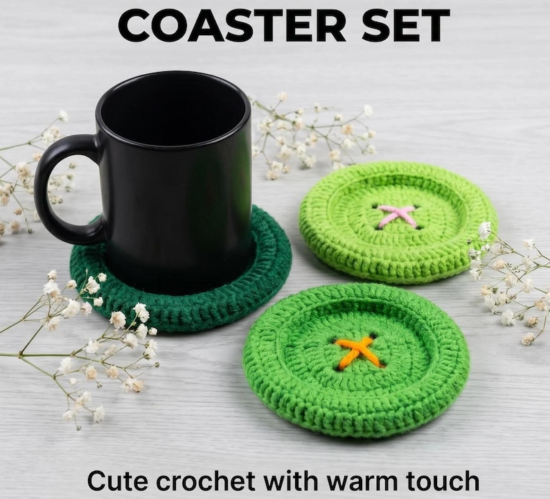 May include: A coaster set featuring three round, button-shaped crochet coasters in shades of dark green and light green. One dark green coaster supports a black ceramic mug. The light green coasters have pink and orange yarn cross-stitch details.