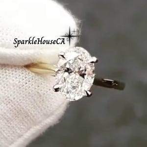 May include: A gold engagement ring featuring a large oval-shaped diamond. The ring is set in a simple band and the diamond is very sparkly.