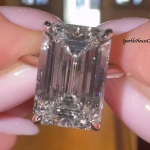 May include: A large, rectangular-cut diamond ring with a gold band. The diamond is held in place by four prongs. The text "SparkleHouseCA" is visible in the background.