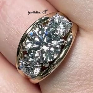 May include: A gold ring featuring three large, clear, round-cut diamonds. The ring has a thick, polished gold band. The diamonds sparkle brightly, reflecting light. The ring is a statement piece of jewelry.