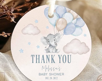 May include: A round baby shower gift tag with a watercolor illustration of a gray elephant holding blue and tan balloons. The tag reads "THANK YOU Melissa's BABY SHOWER DEC. 20, 2022". The tag is tied with a cream-colored ribbon.