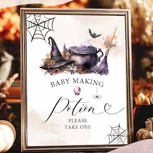 May include: A framed digital print with a Halloween theme. The artwork features a witch's hat, cauldron, broom, and the text "Baby Making Potion." The print includes spiderwebs and a bat, with the text "Please Take One."
