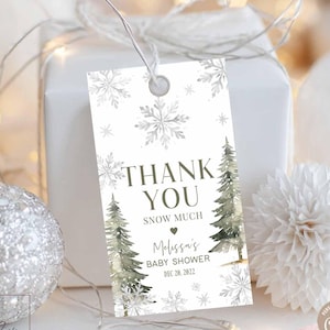 Puede incluir: Una etiqueta de regalo blanca con un diseño de copo de nieve y el texto "THANK YOU SNOW MUCH" con una fecha de baby shower. La etiqueta está adjunta a una caja de regalo blanca, con adornos decorativos.