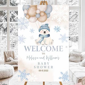 May include: A baby shower welcome sign featuring a polar bear with a blue hat and scarf holding balloons. The sign includes the text "Welcome to Melissa and William's Baby Shower 08.15.2022". The sign is decorated with snowflakes.