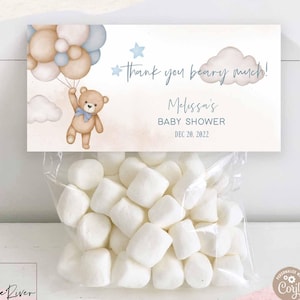 May include: A clear cellophane bag filled with white marshmallows, topped with a baby shower favor tag. The tag features a teddy bear holding balloons, the text "thank you beary much!", and baby shower details.