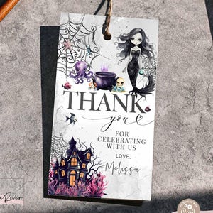 Op de afbeelding: Een rechthoekig papieren cadeaulabel met een gothic zeemeermin, een paarse ketel, een spookhuis en spinnenwebben. De tekst luidt: THANK YOU FOR CELEBRATING WITH US LOVE, Melissa. Het label heeft een bruin touwtje aan de bovenkant om op te hangen.