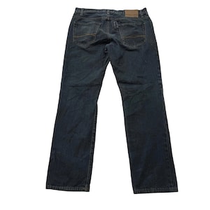 May include: Dark wash denim jeans with a classic five-pocket design. The jeans have a straight leg cut and feature contrasting gold stitching. A brown leather patch is visible on the back waistband.