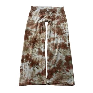 Puede incluir: Pantalones de pernera ancha con teñido anudado en tonos marrón, beige y blanco. Los pantalones tienen cintura con cordón y un ajuste relajado. La tela parece suave y cómoda, adecuada para ropa informal.