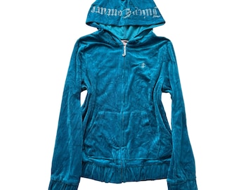 May include: A teal velour zip-up hoodie with a hood featuring the text "Juicy Couture" in silver. The hoodie has a front pocket and the "Juicy Couture" logo on the chest. The jacket is made of a soft, plush material.