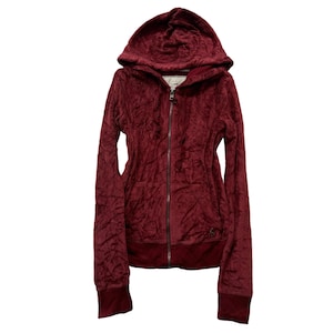 May include: A burgundy hooded zip-up sweatshirt. The jacket has a textured, crushed velvet appearance. It features a full-length zipper, a hood, and ribbed cuffs and hem. The sweatshirt is a solid color with a small logo near the hem.