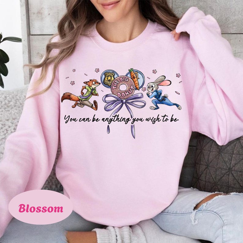 May include: Light pink sweatshirt with a cartoon graphic featuring a fox and a rabbit, with the text "You can be anything you wish to be." The graphic includes a donut and a carrot. The word "Blossom" is printed on the bottom.