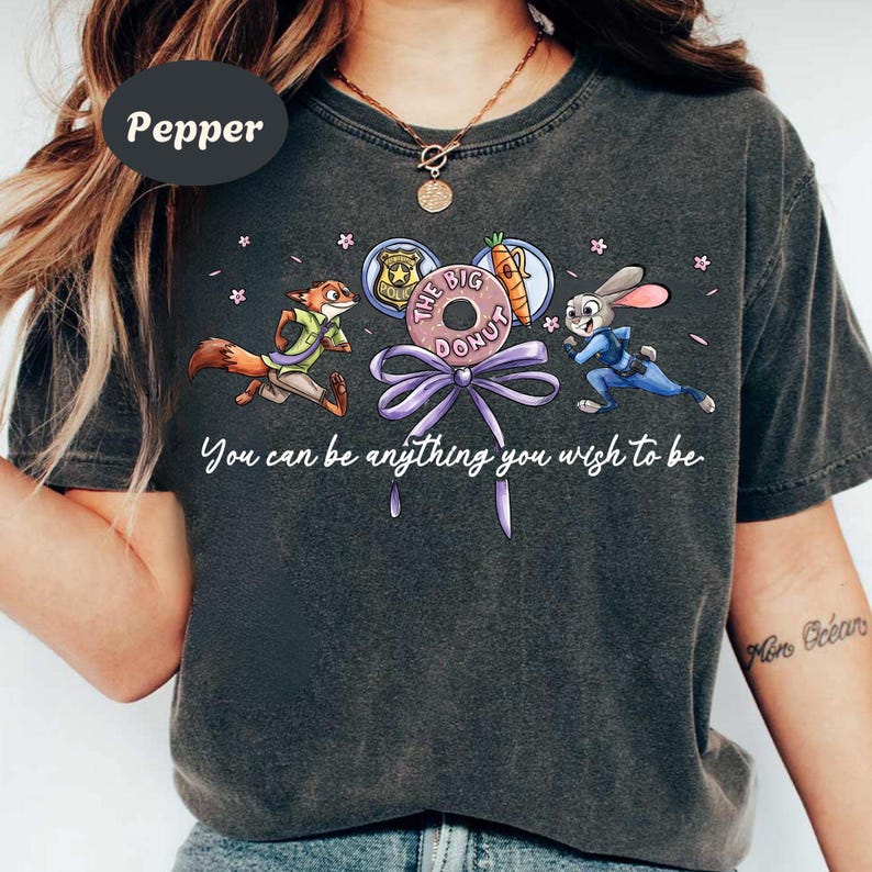 May include: Dark gray t-shirt featuring cartoon characters from Zootopia. The design includes Nick Wilde, Judy Hopps, a donut, and a carrot. The text "You can be anything you wish to be" is also included.