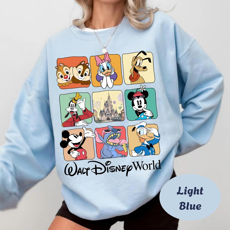 May include: Light blue sweatshirt featuring a grid of Disney characters including Mickey Mouse, Minnie Mouse, Donald Duck, and Stitch. The words "Walt Disney World" are printed in black script. The sweatshirt is a light blue color.
