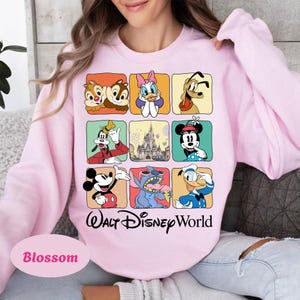 May include: A light pink sweatshirt featuring a grid of Disney characters including Chip and Dale, Daisy Duck, and Mickey Mouse. The words "Walt Disney World" are printed in black script below the grid. The word "Blossom" is printed in a pink oval.