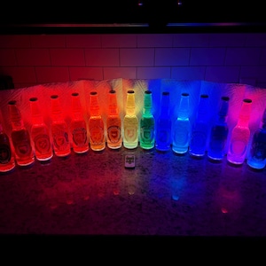 May include: A row of illuminated glass bottles, each emitting a different colour of the rainbow. The bottles are arranged in a spectrum from red to violet. A small remote control is in front of the bottles.