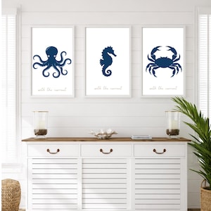 Puede incluir: Tres impresiones artísticas enmarcadas con criaturas marinas azul marino: un pulpo, un caballito de mar y un cangrejo. Cada impresión tiene la frase "with the current". Las impresiones se exhiben sobre un aparador blanco.