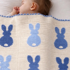 May include: A cream-colored, crocheted baby blanket with a repeating pattern of blue bunny silhouettes. The blanket has a scalloped edge and is draped over a crib. The baby is sleeping.
