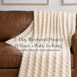 May include: A cream-colored knitted blanket with a textured, woven pattern is draped over a brown leather sofa. The blanket features the text "2-Day Weekend Project" and "8 Sizes - Baby to King". The image suggests a cozy home decor item.