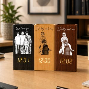 Peut inclure: Trois horloges de bureau rectangulaires en bois avec des affichages numériques indiquant 12:01, 12:00 et 12:02. Chaque horloge présente une photo et un texte gravés au laser. L'horloge de gauche est noire, celle du centre est en bois clair.