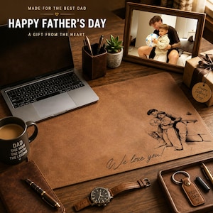 May include: A brown leather desk mat featuring an engraved illustration of a person holding a child and the text "We love you!". The mat is displayed on a desk with a laptop, a mug with "DAD THE MAN THE MYTH THE LEGEND" text, a watch, and a keychain.