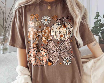 May include: Brown t-shirt with a fall-themed graphic. The design features pumpkins, bows, daisies, and leaves in shades of orange, white, and brown. The text "Comfort Colors Espresso" is printed at the bottom.