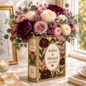 May include: A rectangular book-shaped vase featuring a stained-glass style floral pattern with the text "The Beginning of Forever," "Ashley & Michael," "09.14.2026," and "Est. 2026." The vase is filled with a large bouquet of pink, white, and dark red flowers.
