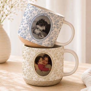 May include: Two ceramic mugs stacked vertically, each featuring a custom oval photo frame surrounded by a floral pattern. The top mug has a blue floral design with a black and white photo, while the bottom mug has a tan floral design with a color photo.