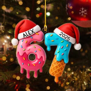 May include: Two Christmas ornaments shaped like the numbers 6 and 7. The number 6 is pink and donut-shaped with the name "ALEX" on a Santa hat. The number 7 is blue with a waffle cone base and the year "2025" on a Santa hat.