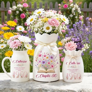 May include: A white ceramic mug and two white ceramic vases filled with colorful flowers. The mug and one vase feature the text Catherine, Making the world a better place since 1950. The central vase features an open book and Chapter 80.