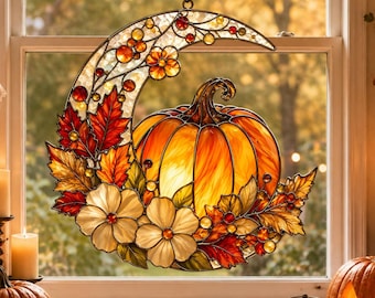 May include: A stained glass suncatcher shaped like a crescent moon featuring a central orange pumpkin, red and orange autumn leaves, and white flowers. The piece is constructed with dark metal lead lines and hangs by a chain in a window.