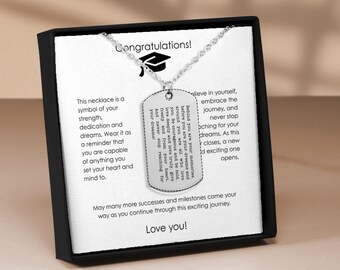 May include: A silver-colored dog tag necklace with a graduation cap charm. The tag has engraved text about dreams and strength. The box has the text "Congratulations!" and "Love you!"