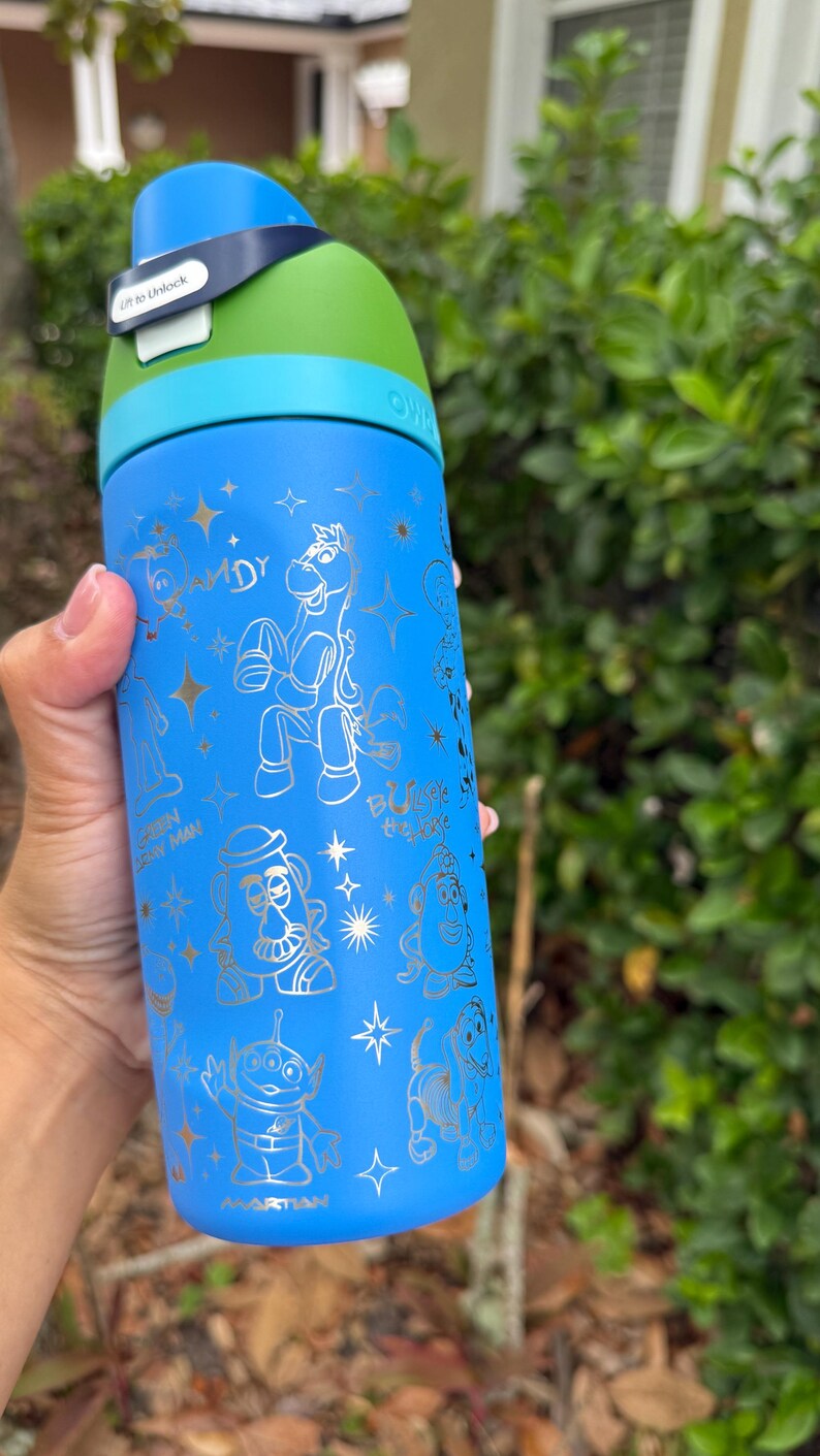 May include: Blue water bottle with a green and blue lid. The bottle features gold illustrations of characters from a popular animated movie. The text "Lift to Unlock" is visible on the lid.