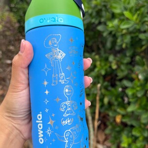 May include: Blue Owala water bottle with a green lid and a blue handle. The bottle features silver illustrations of characters from a popular animated film. The word "owala" is printed on the bottle.