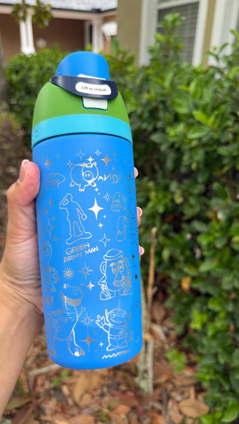 May include: Blue water bottle with a green and blue lid. The bottle features gold illustrations of characters and phrases from the movie Toy Story. The lid has the text "Lift to Unlock".