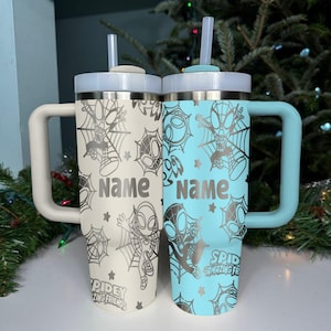 Puede incluir: Dos vasos aislados con asas, uno blanquecino y otro azul claro. Cada uno presenta un dise&ntilde;o de Spider-Man con una telara&ntilde;a, estrellas y la palabra "Name". El vaso azul claro tambi&eacute;n tiene el texto "Spidey and Amazing Friends".