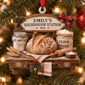 May include: A decorative Christmas ornament shaped like a wooden shelf labelled EMILY'S SOURDOUGH STATION 2026. It features a loaf of bread, a jar labelled Sourdough Starter, a sack labelled FLOUR, a wooden rolling pin, and wheat stalks.