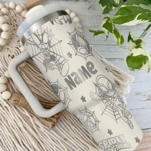 Puede incluir: Un vaso t&eacute;rmico blanco con asa, con gr&aacute;ficos de Spiderman y la palabra "Name". El dise&ntilde;o incluye a Spiderman, telara&ntilde;as y estrellas. Tambi&eacute;n es visible el texto "Spidey Amazing Friends".
