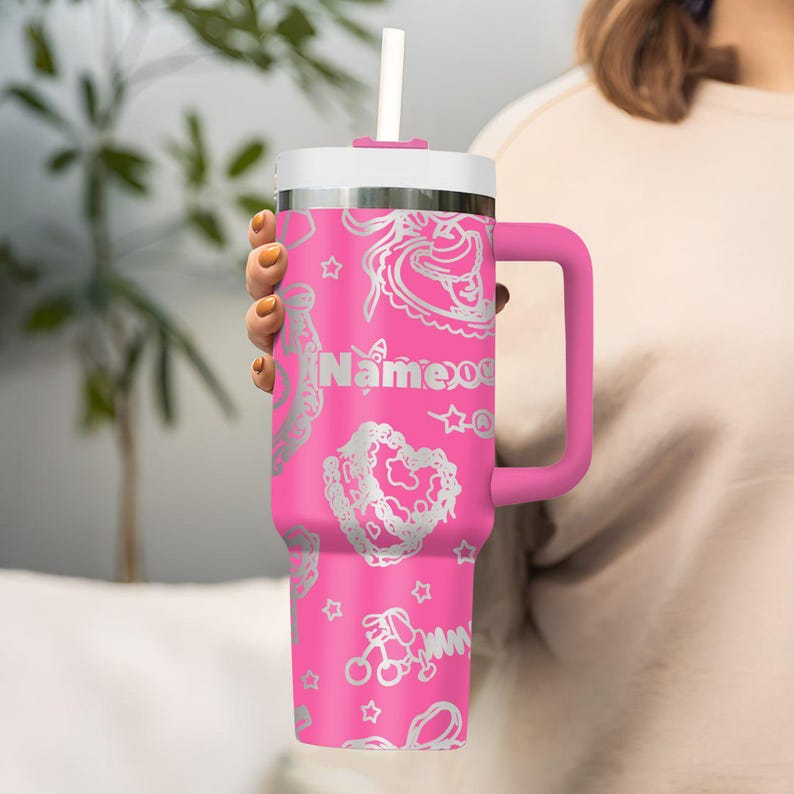 May include: A pink insulated tumbler with a white lid and handle, featuring a silver pattern of hearts, stars, and other designs. The tumbler includes a white straw and the name "Name09" in silver lettering.
