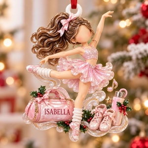 May include: A hanging ornament featuring a dancer with brown hair and a pink glittery outfit. Below the dancer is a pink duffel bag with the name ISABELLA printed on it, a pair of pink sneakers, a pink water bottle, and holly berry accents.