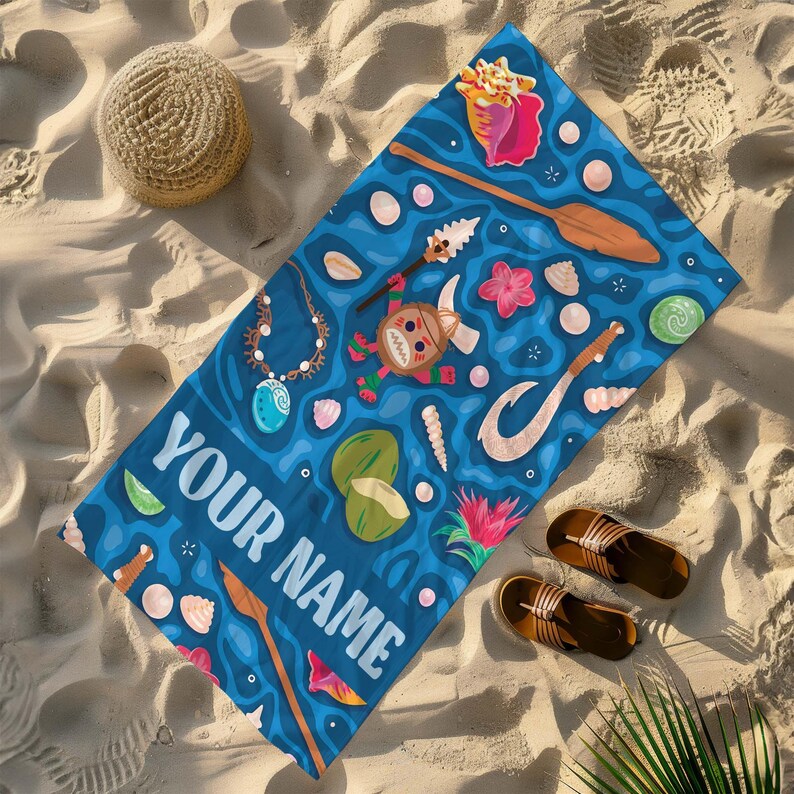 Pode incluir: Uma toalha de praia azul com um design tropical com conchas, cocos e uma personagem de desenho animado. A toalha tem o texto "YOUR NAME" em branco. Um chap&eacute;u de palha e sand&aacute;lias est&atilde;o ao lado da toalha na areia.