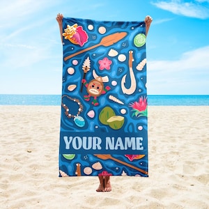 Pode incluir: Uma toalha de praia azul com um design tropical com conchas, um remo de madeira, um anzol e uma personagem de desenho animado. A toalha tem o texto "YOUR NAME" em letras brancas na parte inferior. O fundo &eacute; o oceano e o c&eacute;u.