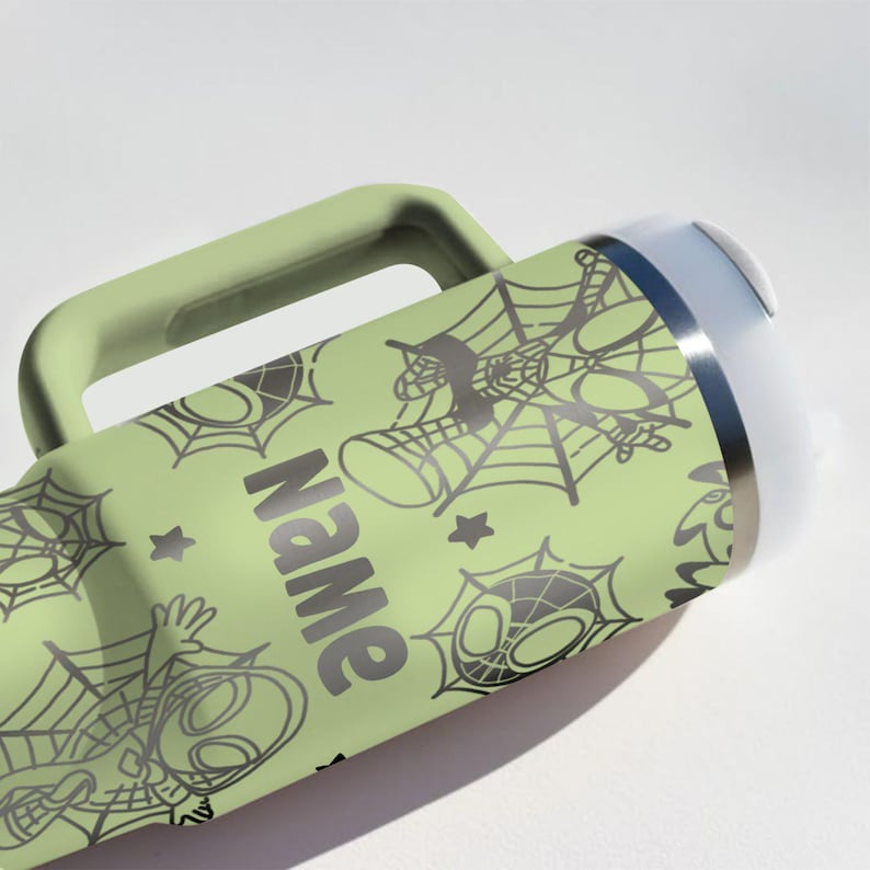 Puede incluir: Una botella de agua verde claro con asa, con un patr&oacute;n repetido de telara&ntilde;as y una ara&ntilde;a de dibujos animados. La palabra "Name" est&aacute; impresa en el lateral en gris oscuro. La botella tiene un borde plateado y una parte superior blanca.