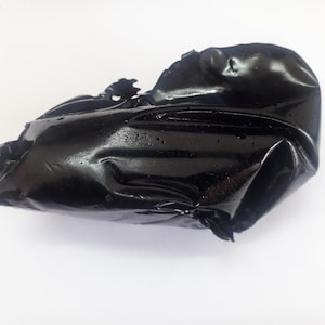 May include: A shiny, black, shapeless object with a reflective surface. The object has an irregular form with folds and creases, and appears to be made of a pliable material. The background is plain white.