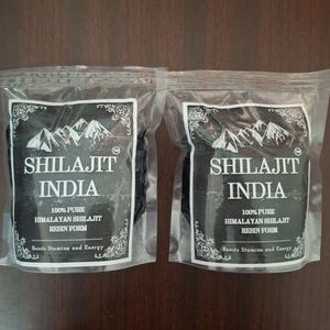 May include: Two sealed packages of Shilajit resin from India. Each package has a black label with white text and a mountain range graphic. The label reads "100% Pure Himalayan Shilajit Resin Form" and "Boosts Stamina and Energy."