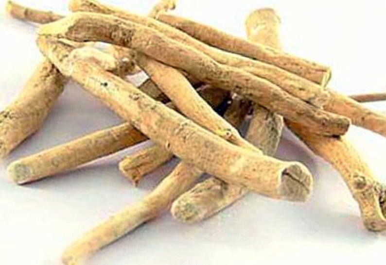 May include: A close-up shot of several light brown, dried ashwagandha roots. The roots are cylindrical, with a rough texture and varying thicknesses. Some roots have a lighter, almost beige color, while others are a darker brown.