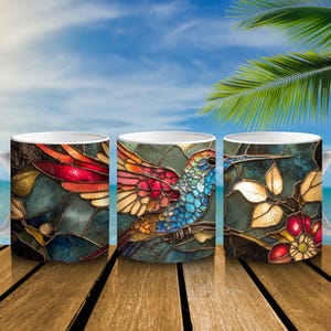 Puede incluir: Tres tazas de cerámica blanca con un diseño de vidriera que presenta un colibrí, flores y follaje. El colibrí tiene plumas rojas, azules y amarillas. El fondo es de color verde azulado con una escena de playa.