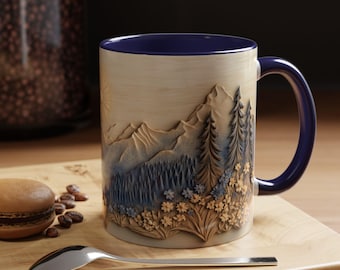May include: A ceramic mug featuring a mountain and forest relief design. The mug has a blue interior and handle, with a beige exterior. A spoon and a macaron are on a wooden surface.